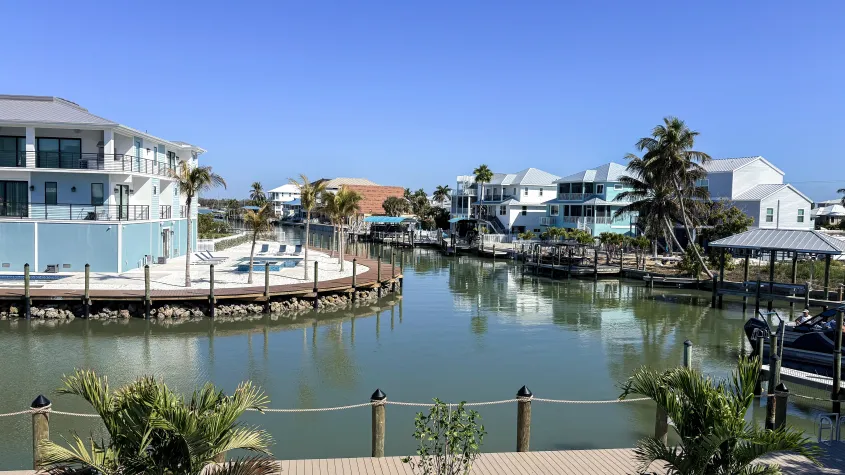 overlooking water, white fence, palm trees, houses, blue skies, a boat dock