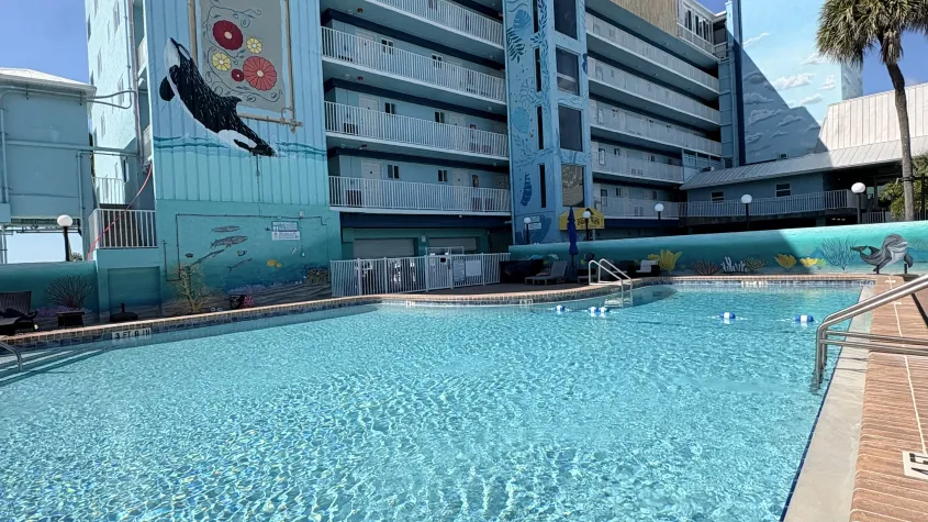pool with hotel building behind it blue skies and clouds