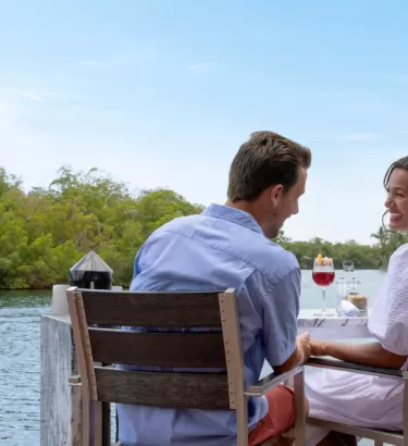 A man and a woman enjoy a meal outside at table alongside a canal